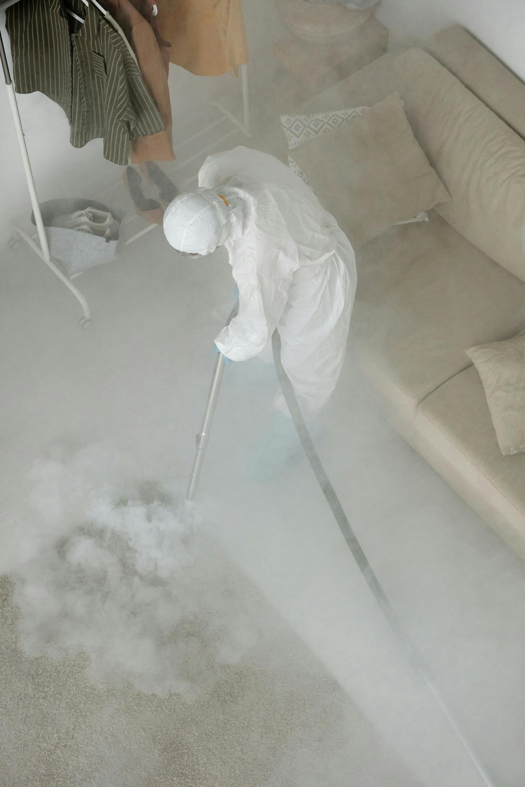 A person in a white protective suit fumigating an indoor space with smoke.